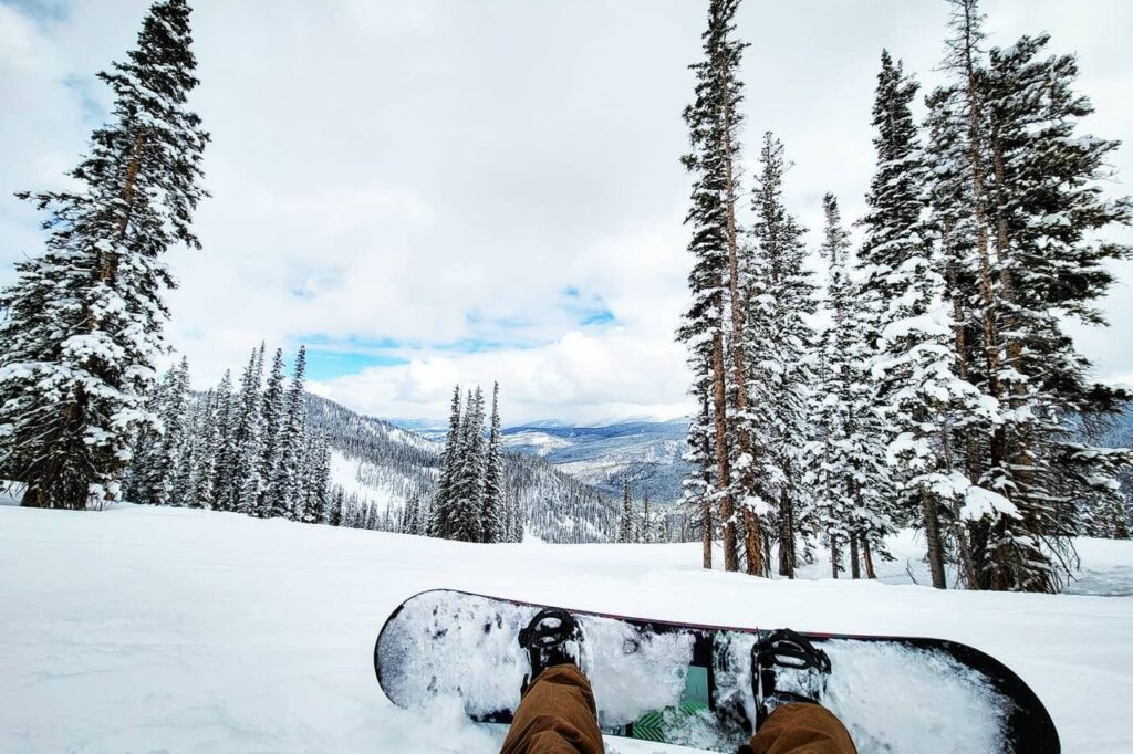 A person is snowboarding on a snowy slope in Winter Park with trees in the background.