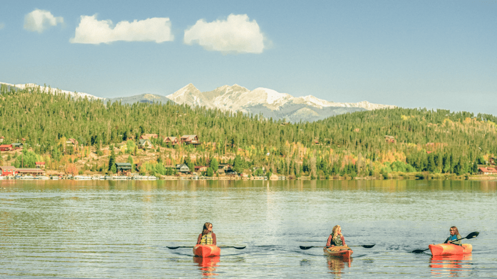 Three people paddling canoes on a lake with mountains in the background.