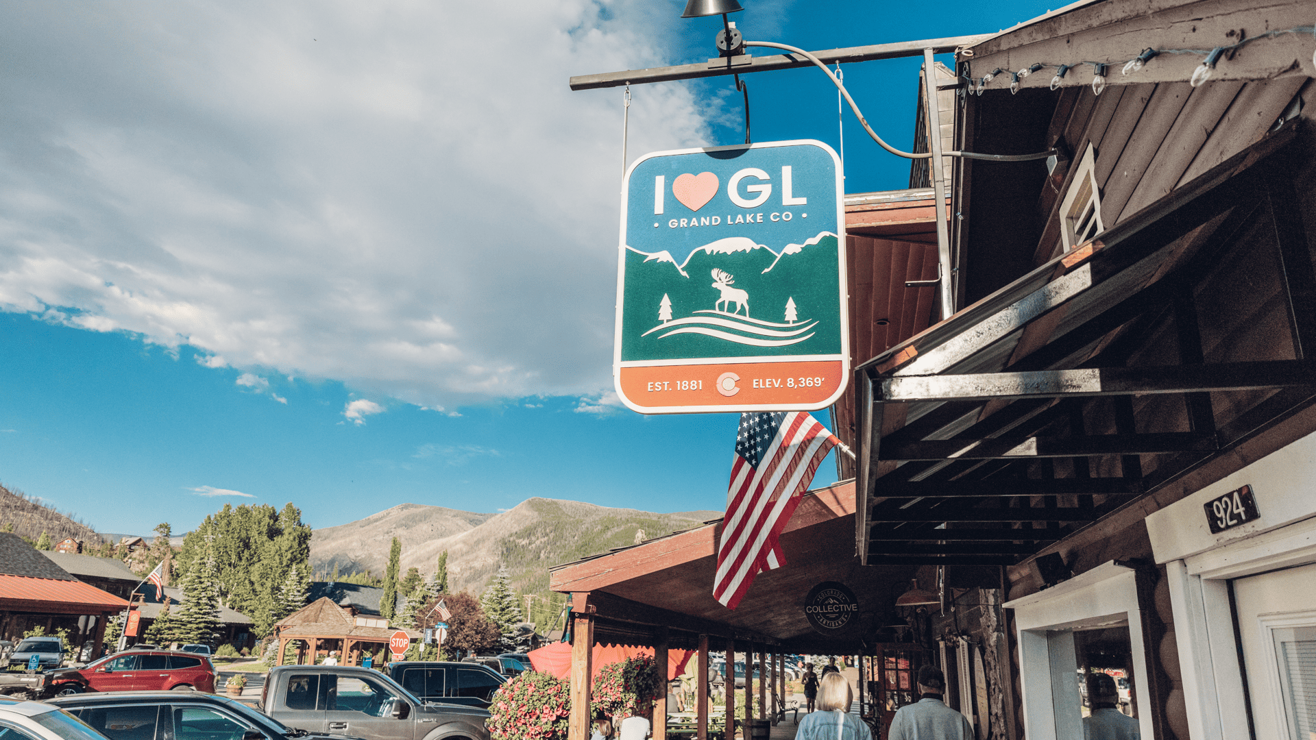 A sign that says "I Love Grand Lake, CO" hands on a building in downtown Grand Lake, with mountains from Rocky Mountain National Park in the background