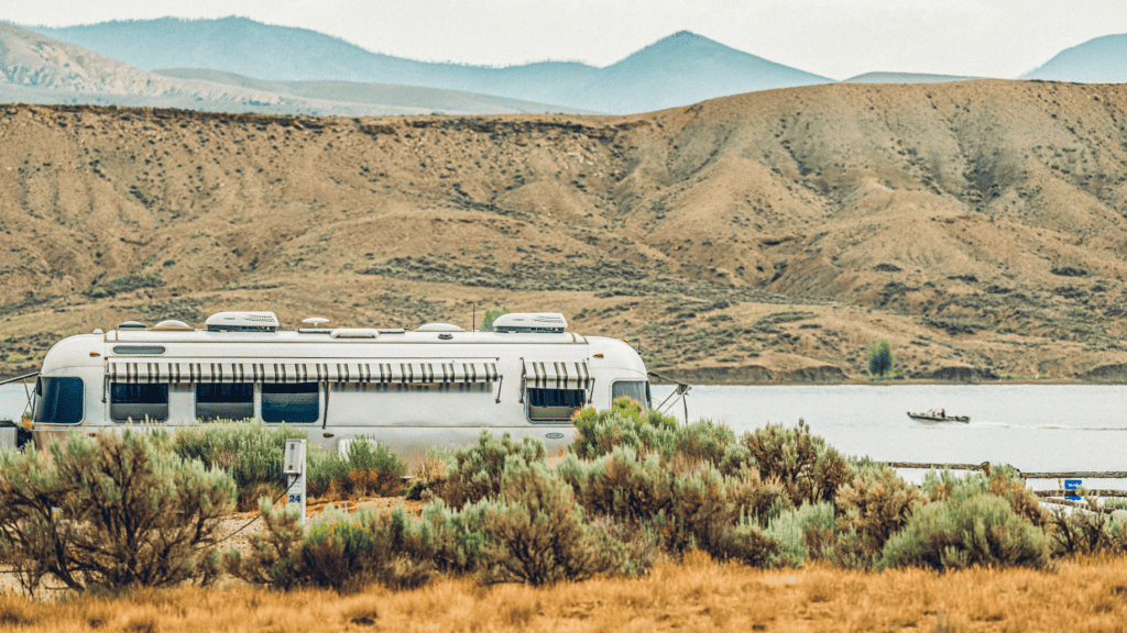 An rv parked near a lake with mountains in the background.