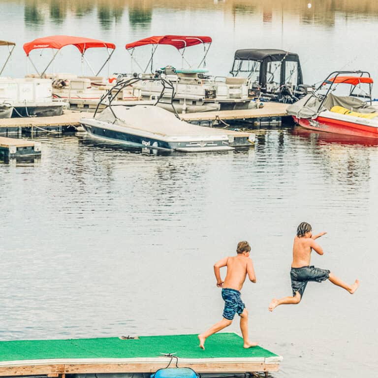 Two boys jumping off a dock into a body of water.