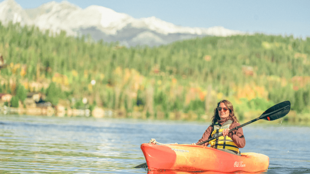 A woman kayaking on a lake with mountains in the background.