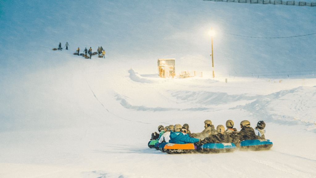 A group of people riding sleds down a snowy hill.