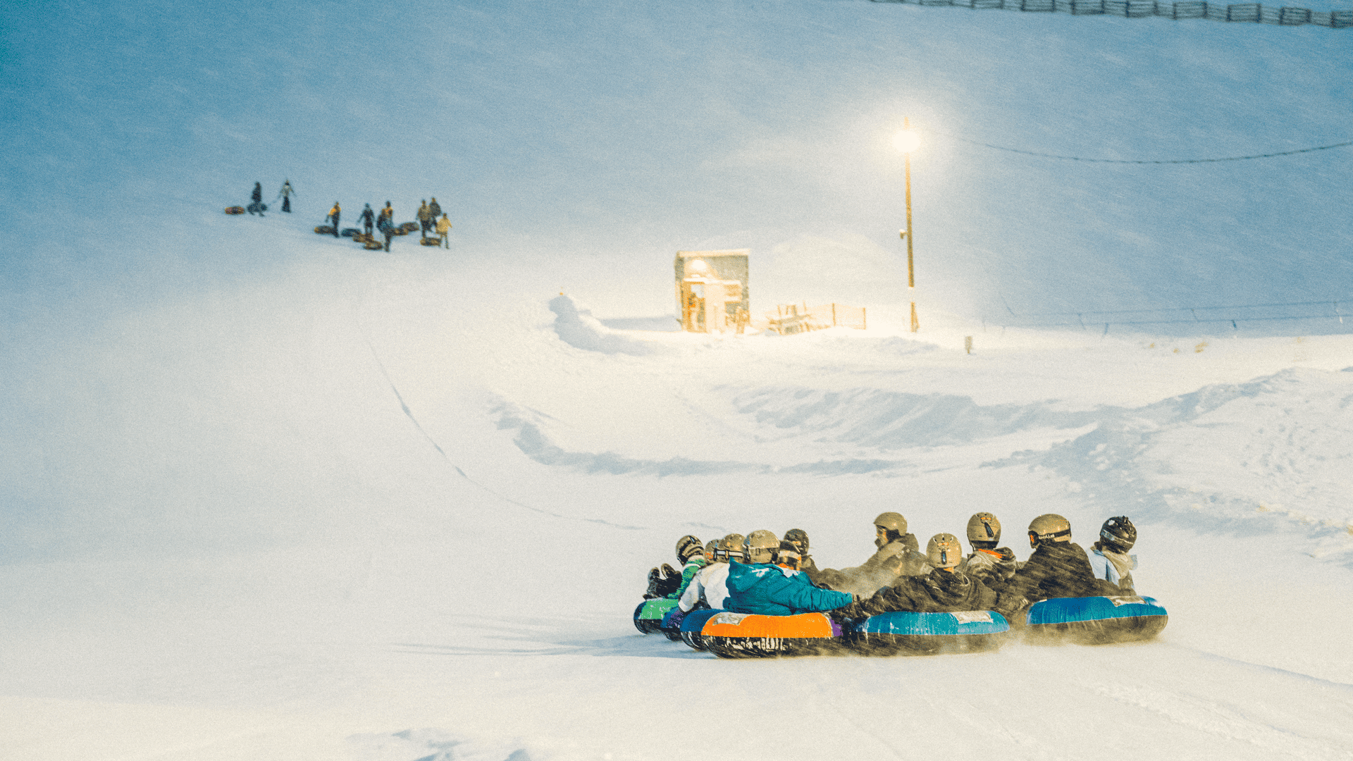 A group of people riding sleds down a snowy hill.