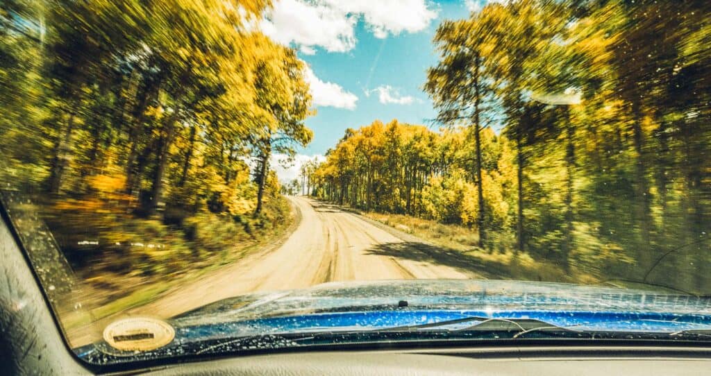A car driving down a dirt road with trees in the background.