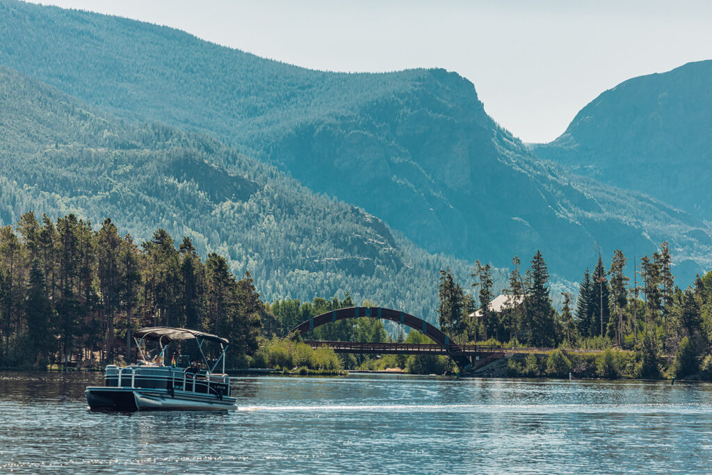 A boat moves across Grand Lake in the direction of evergreen-covered hills.