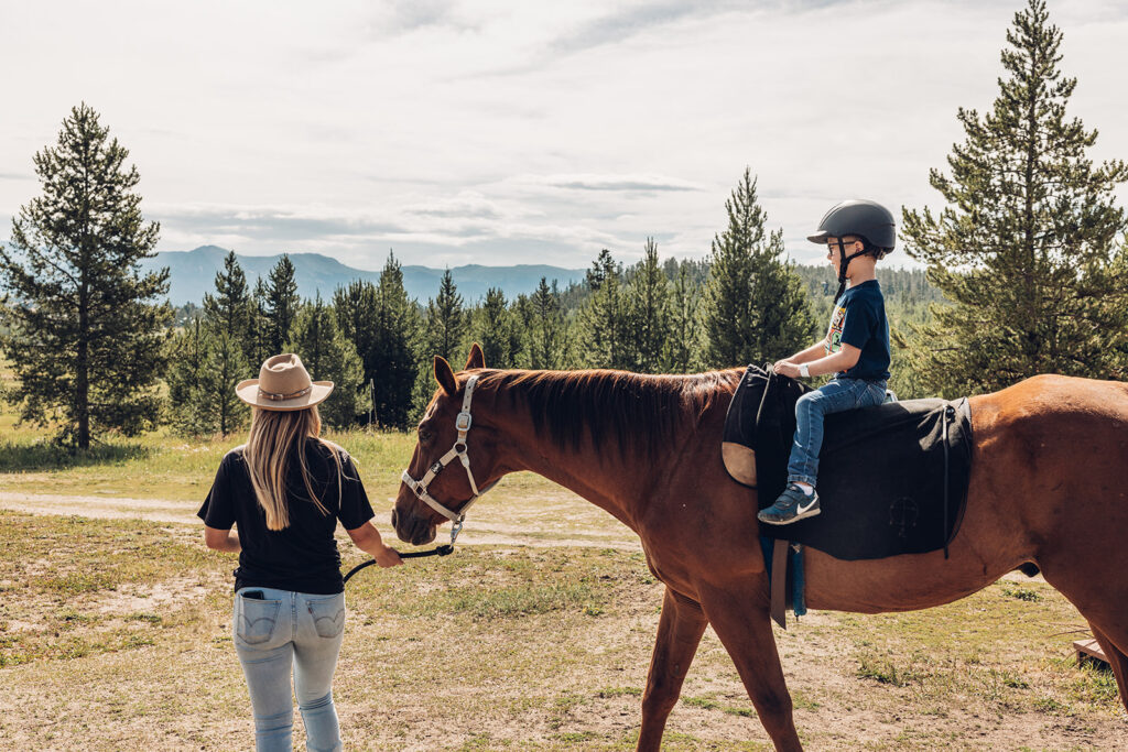 A woman is riding a horse with a child in the background.