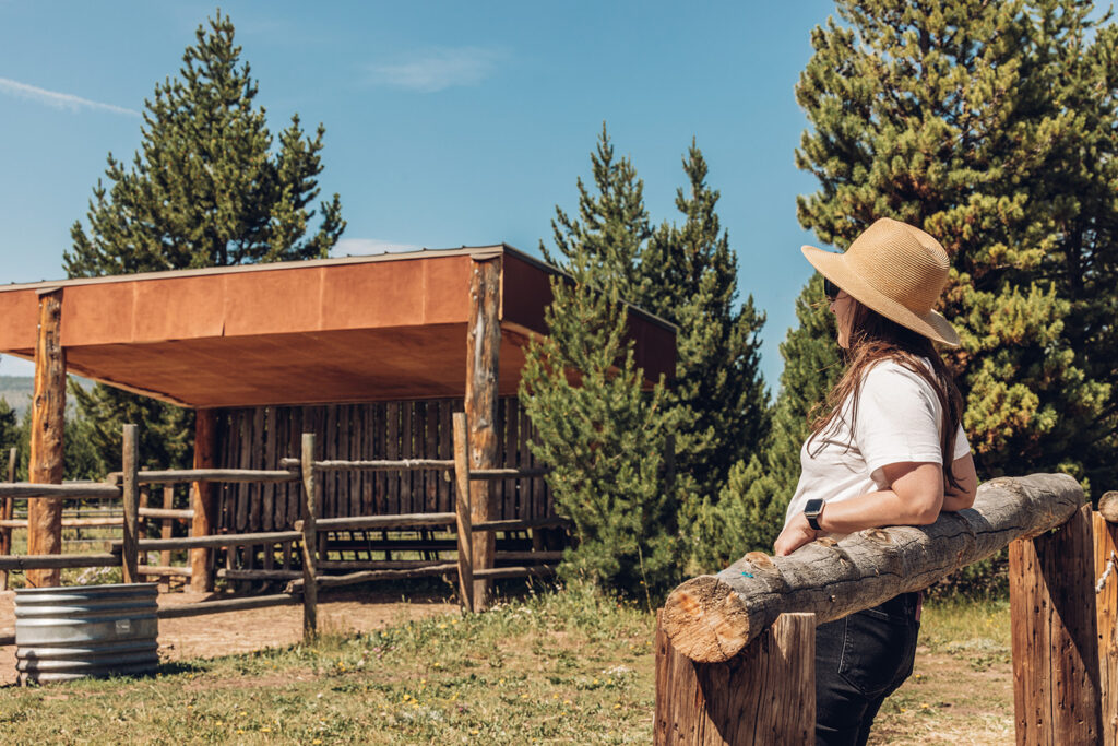 A woman in a hat is standing on a wooden fence.