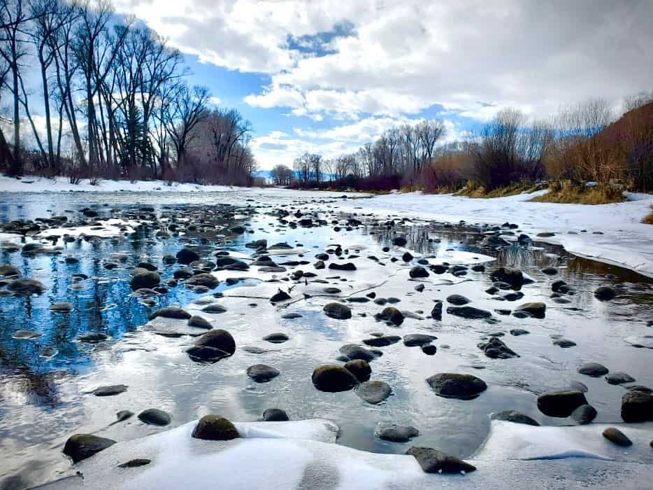 A frozen river with rocks and trees in the background.