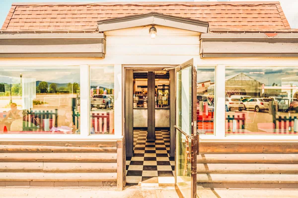 Windows reflect the blue sky at the entrance to Debbie's Drive In diner. Through the door you can see a checkered floor.