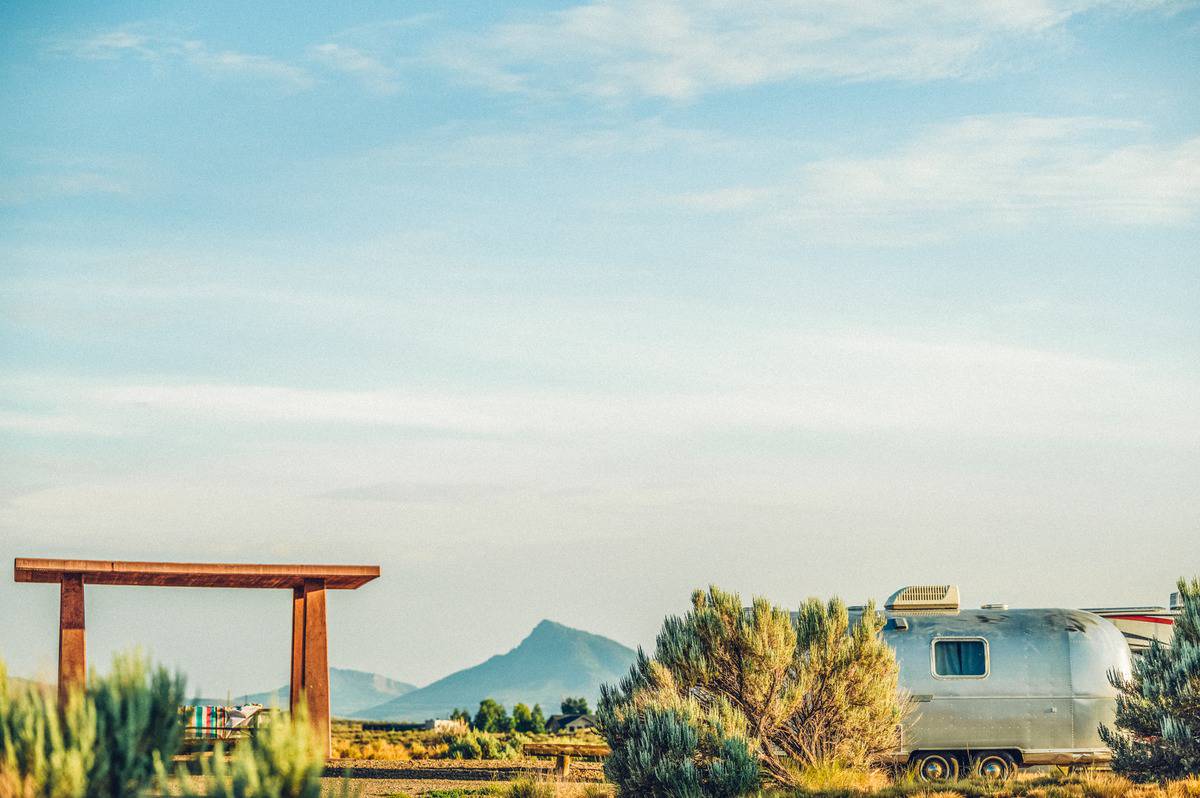 A metal airstream camper sits at a campground surrounded by sagebrush in Kremmling, Colorado with the Rocky Mountains in the background.