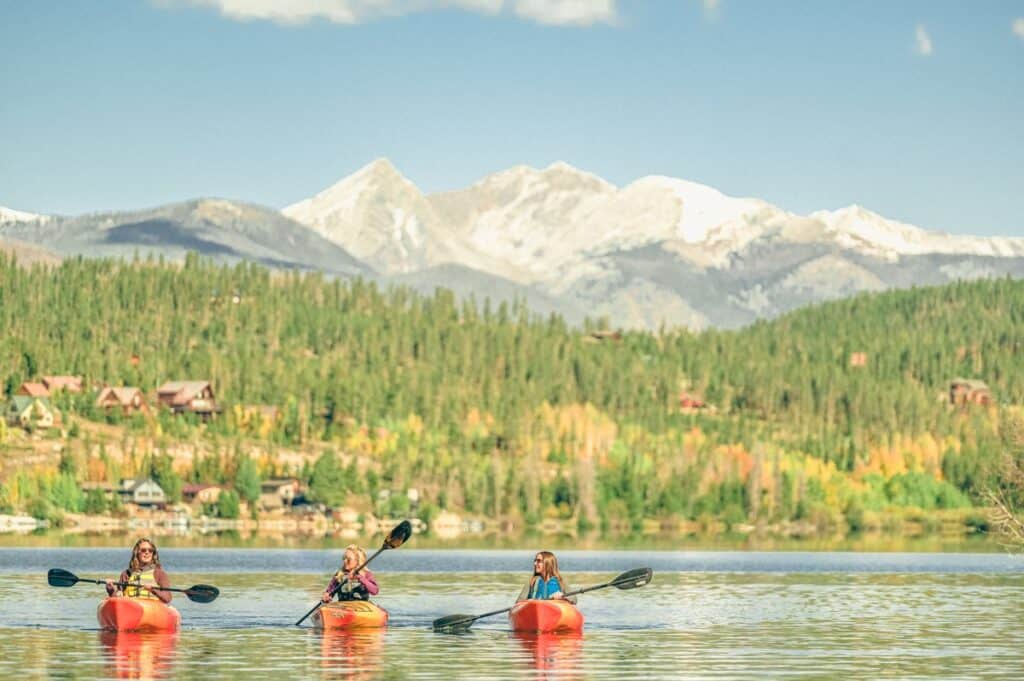Three people kayaking on Grand Lake, Colorado, with stunning mountain views of Rocky Mountain National Park in the background.