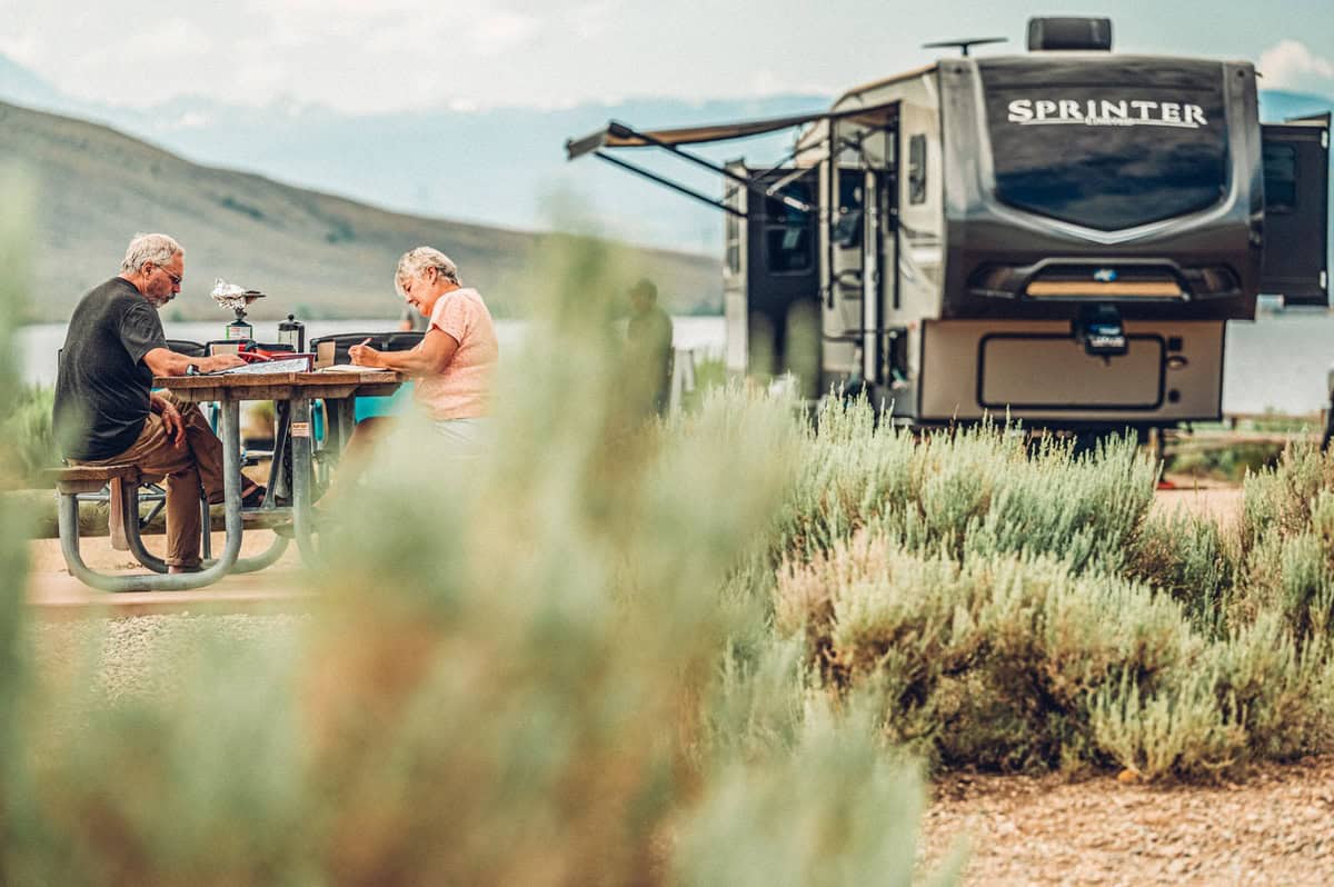 A family sits at a picnic table at a Lake Granby campsite, looking at a map with an RV parked in the background