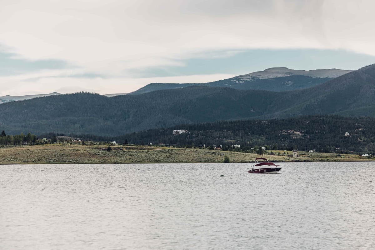 A motor boat sits on Lake Granby with a campsite and mountains in the background