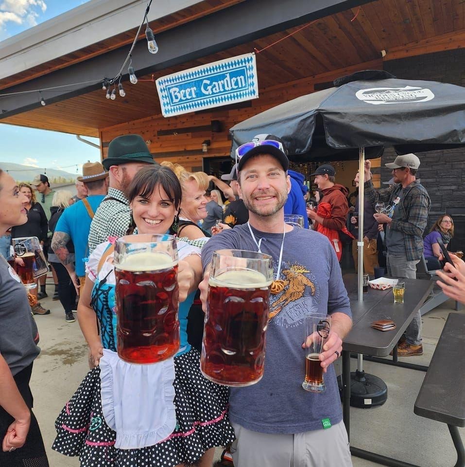Two people dressed in traditional German attire hold large steins of beer at an outdoor event in Grand County Colorado.