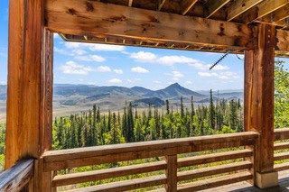 A wooden deck with a railing overlooks a vast forest and distant mountains under a clear blue sky in Grand County Colorado.