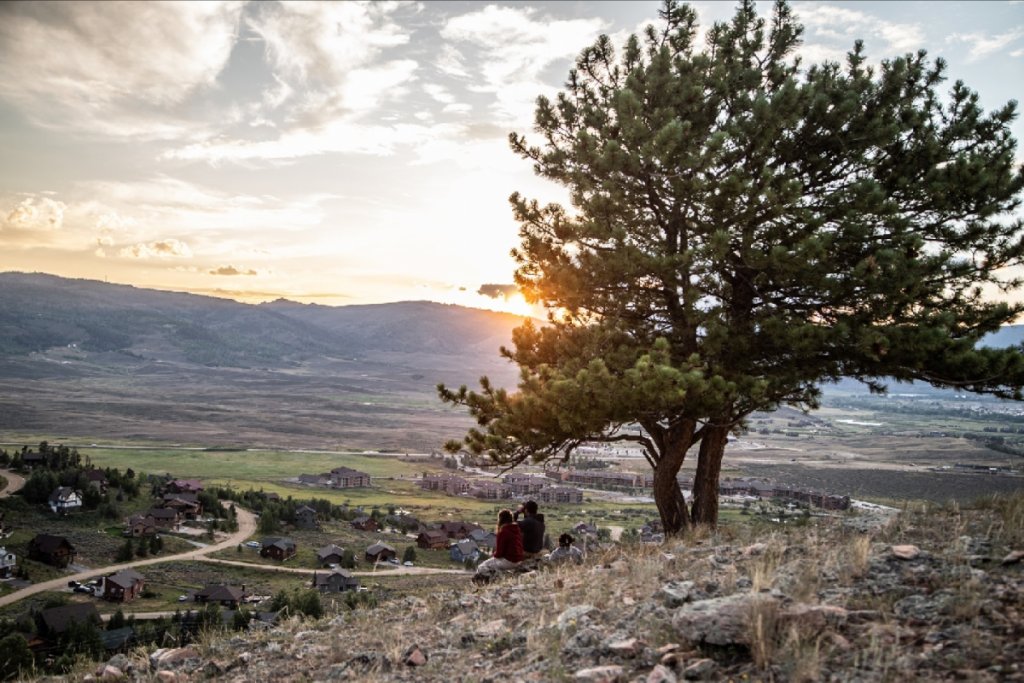 A couple sits on a rocky hill at sunset, gazing at a sprawling valley with houses and distant mountains in Grand County Colorado.