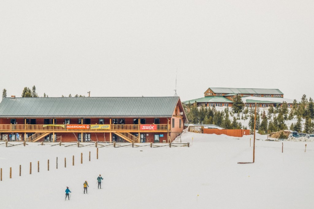Skiers glide across snowy terrain near a rustic lodge with colorful signage in Grand County Colorado.