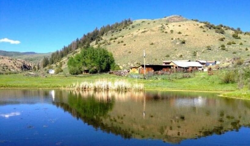 A serene pond reflects a mountain landscape with a rustic cabin and lush greenery in Grand County Colorado.