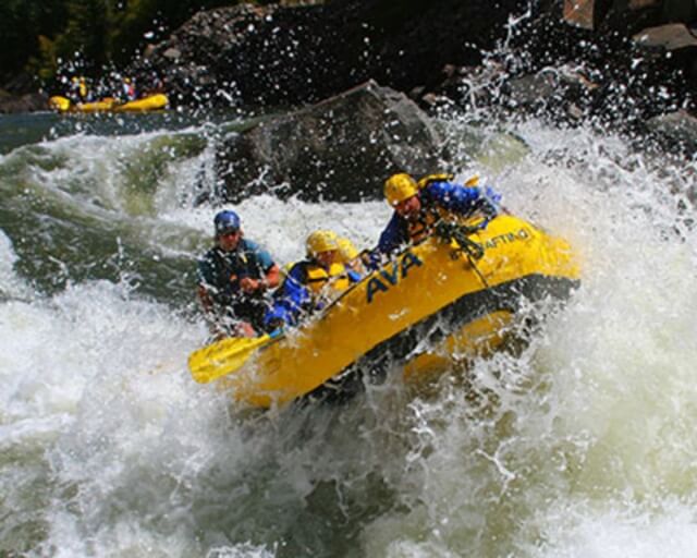 A group of four people navigate a yellow raft through white water rapids in Grand County Colorado.