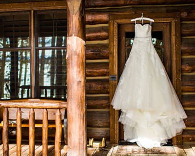A white wedding dress hangs on a wooden door of a rustic log cabin in Grand County Colorado.