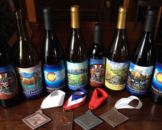 A row of colorful wine bottles with animal and nature labels, accompanied by medals and ribbons in Grand County Colorado.