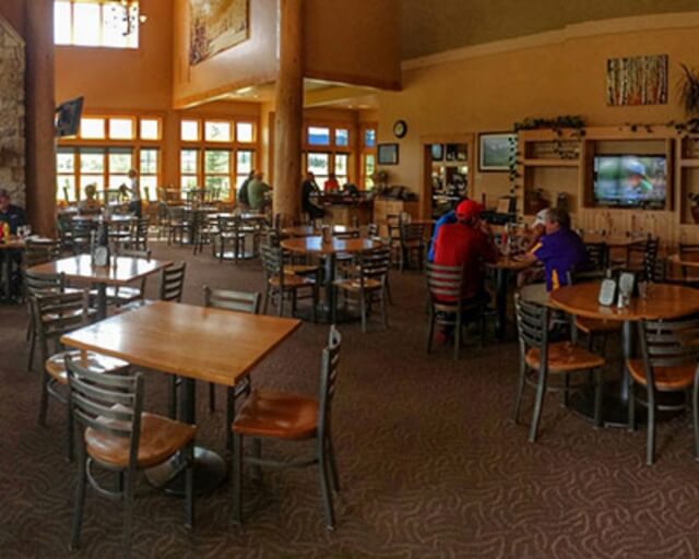 A spacious restaurant with wooden tables, chairs, and a stone fireplace in Grand County Colorado.