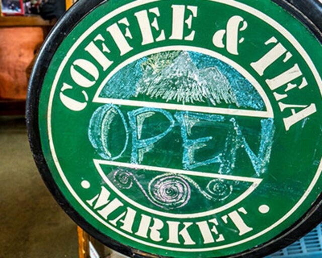 A green circular sign with white text advertising a coffee and tea market, featuring a mountain illustration in Grand County Colorado.