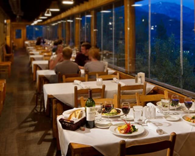 A dimly lit restaurant with large windows offers a view of the mountains while patrons dine in Grand County Colorado.