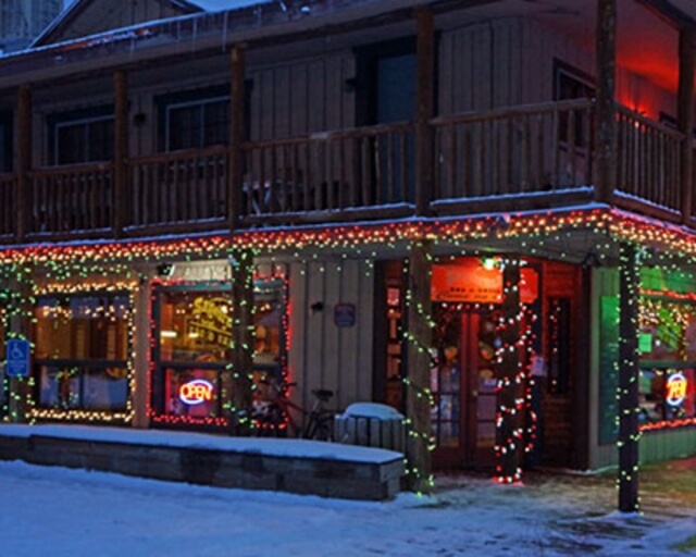 A cozy wooden building adorned with festive lights and snow, featuring a welcoming sign in Grand County Colorado.