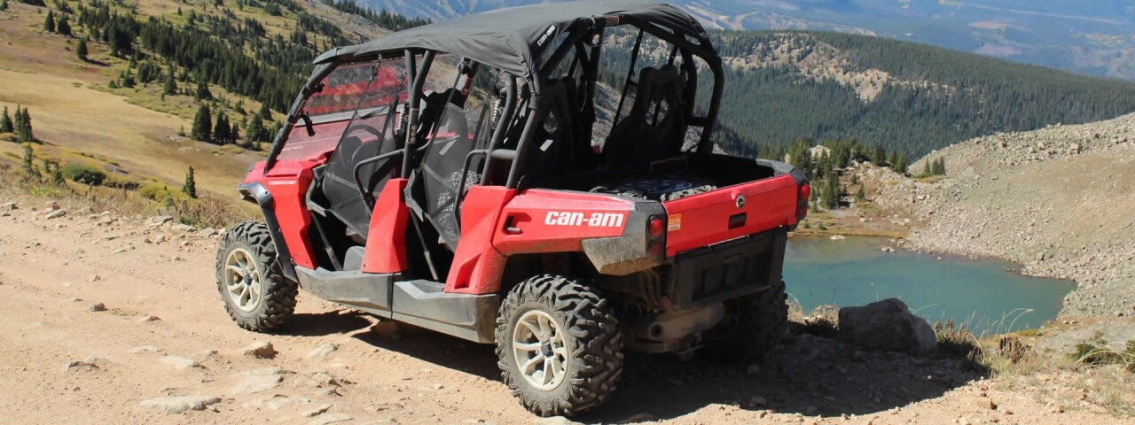 Red Can-Am off-road vehicle parked on rocky terrain near a serene mountain lake in Grand County Colorado.