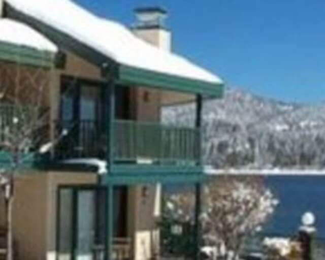 A snow-covered house with a balcony overlooks a serene lake surrounded by mountains in Grand County Colorado.