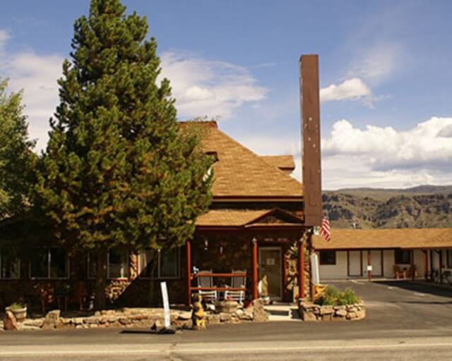 A rustic lodge with a stone fireplace and a tall chimney is nestled among tall pine trees in Grand County Colorado.
