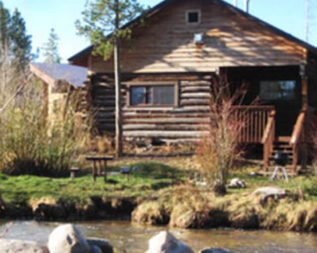 Rustic log cabin nestled in a wooded area beside a small stream in Grand County Colorado.