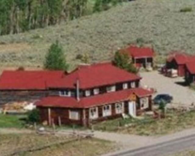 A rustic red-roofed lodge with multiple buildings nestled in a grassy valley surrounded by trees in Grand County Colorado.