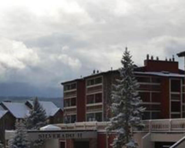 A snowy mountain resort with a red building and snow-covered trees under a cloudy sky in Grand County Colorado.