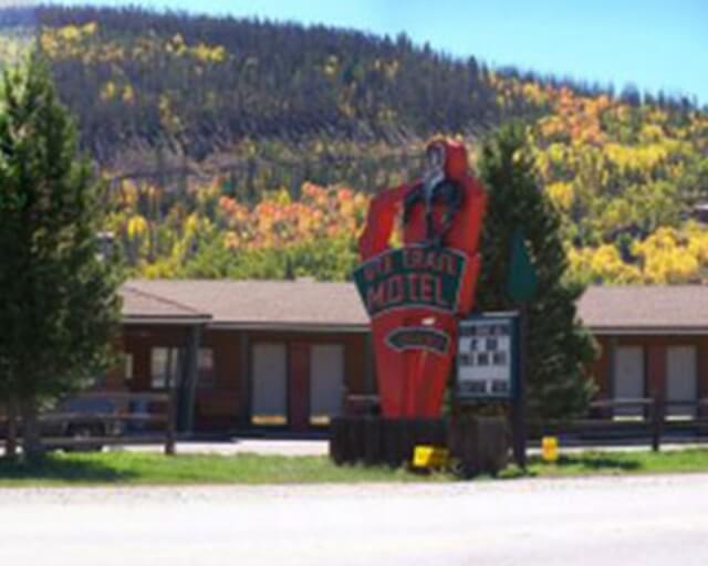 A vintage motel sign with a red figure stands in front of a colorful autumn forest in Grand County Colorado.