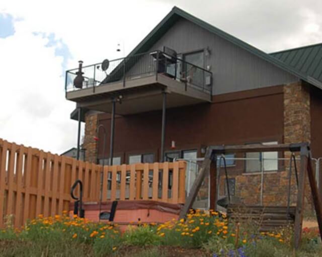A two-story house with a balcony, stone accents, and a fenced yard with a swing set in Grand County Colorado.