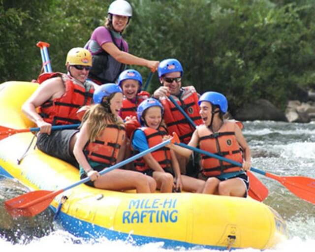 A group of people, including children, are rafting down a river in a yellow inflatable raft in Grand County Colorado.