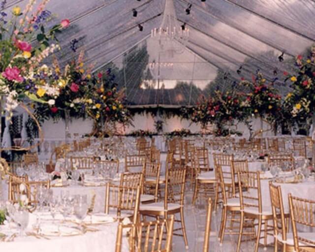 Elegant wedding reception with gold chairs, floral centerpieces, and a chandelier in a clear tent in Grand County Colorado.