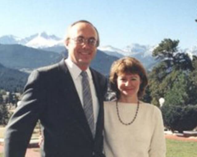 A man and woman stand together outdoors, smiling, with mountains in the background in Grand County Colorado.