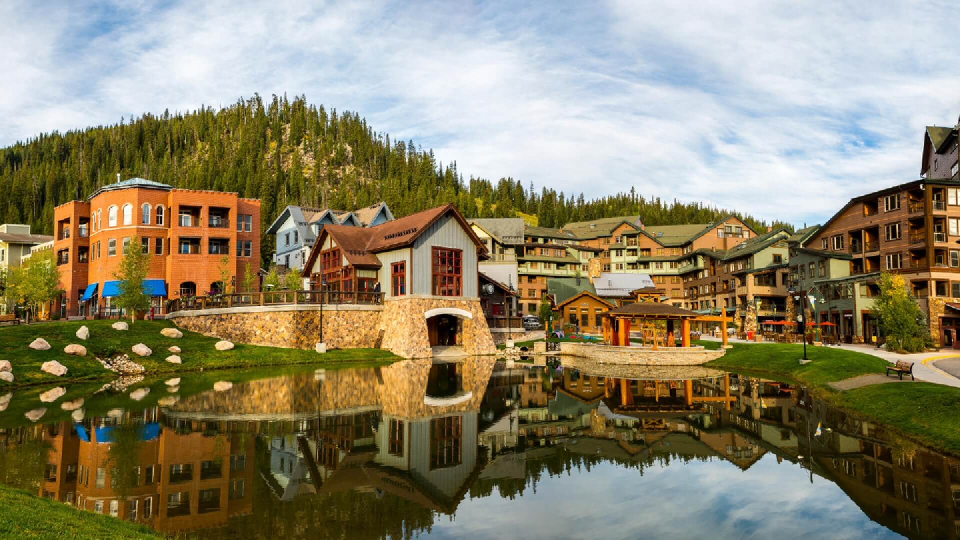 A serene mountain village with colorful buildings reflected in a calm pond in Grand County Colorado.