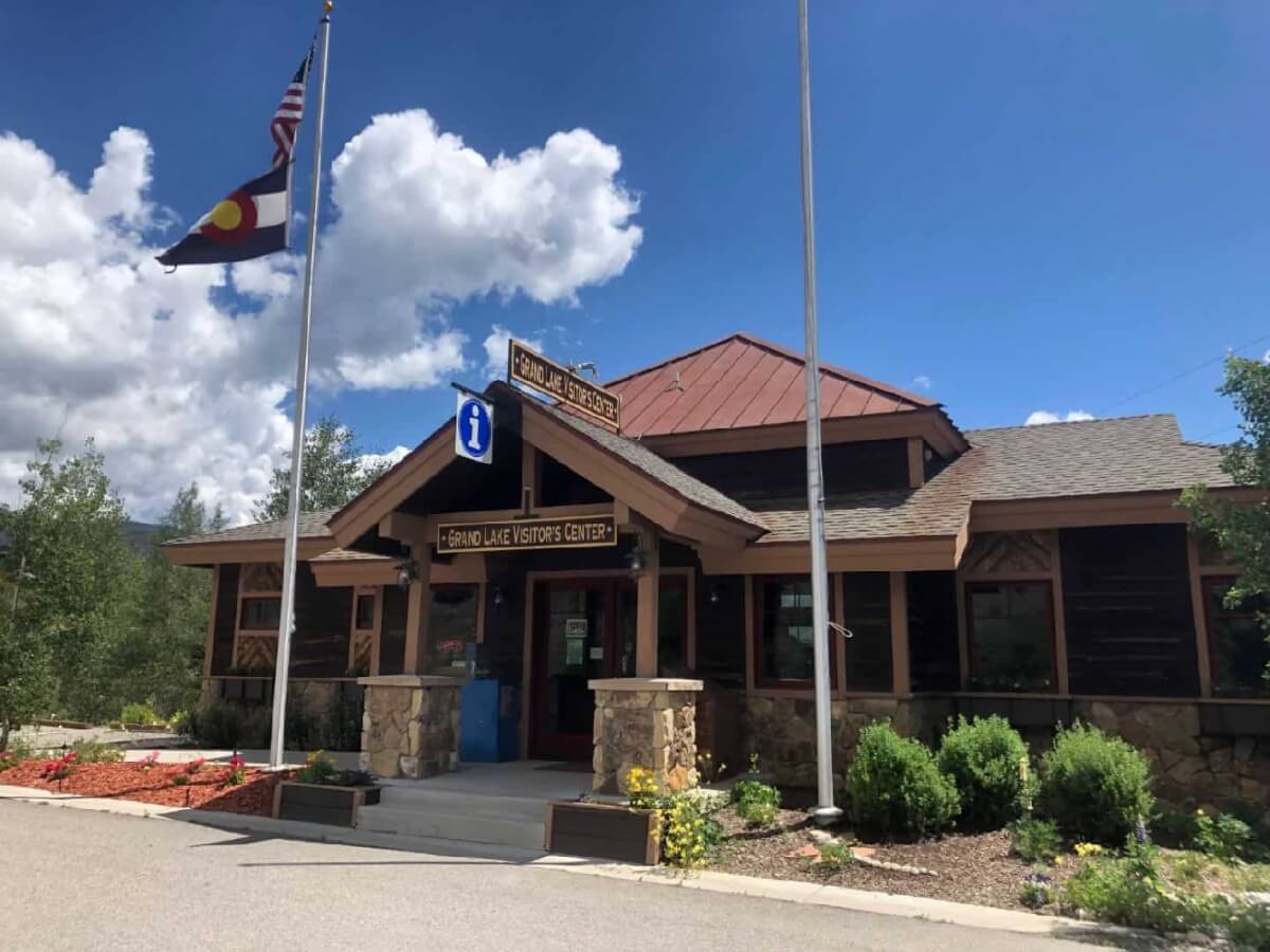 A rustic visitor center with stone pillars and a wooden roof, surrounded by greenery and flags in Grand County Colorado.