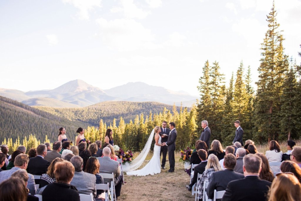 A wedding ceremony takes place outdoors with a couple standing in front of a mountain backdrop in Grand County Colorado.