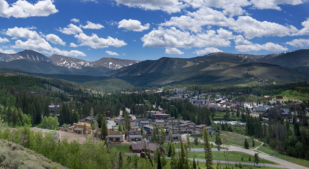 Scenic view of Winter Park with lodge buildings nestled among pine trees and mountains in the background.