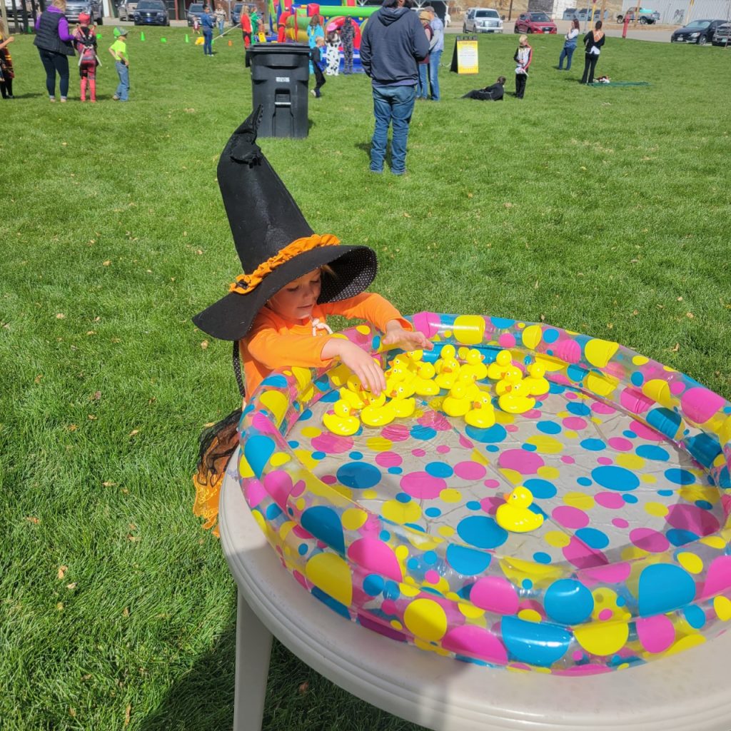 A young child in a witch costume sits at a table playing with rubber ducks in a colorful pool in Grand County Colorado.