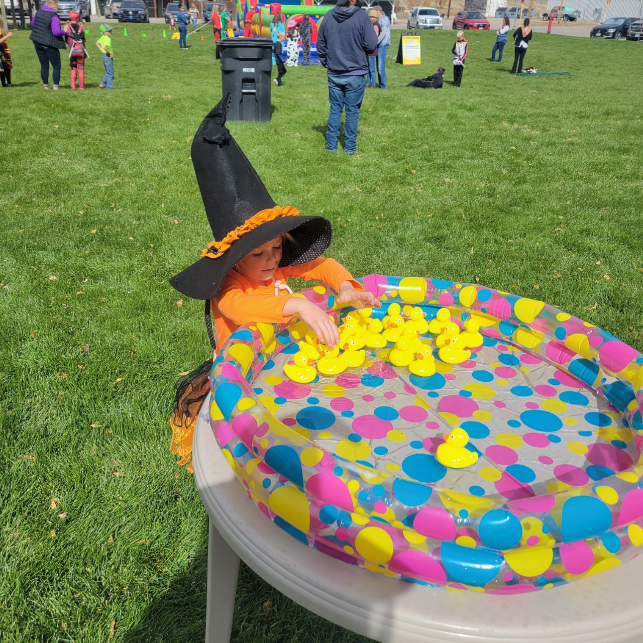 A young child in a witch costume sits at a table playing with rubber ducks in a colorful pool in Grand County Colorado.