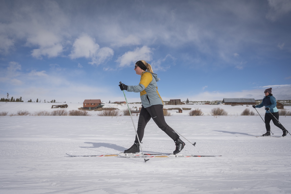 Two women cross-country skiing on a snowy landscape with mountains in the distance in Grand County Colorado.