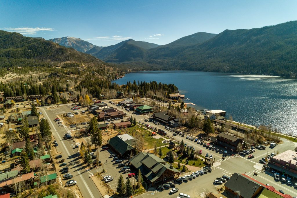 Aerial view of a mountain town with a lake, surrounded by forests and snow-capped peaks in Grand County Colorado.