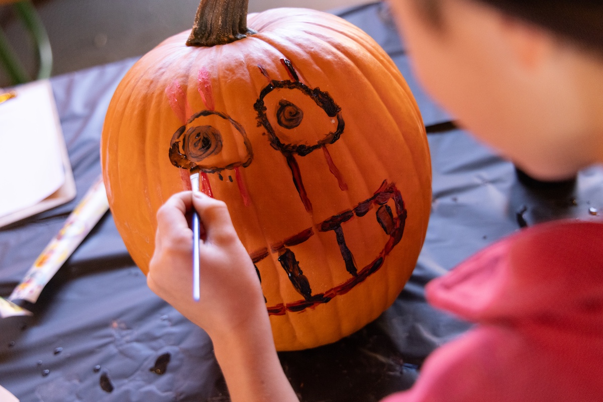 A child paints a smiling jack-o'-lantern face on an orange pumpkin with black paint in Grand County Colorado.